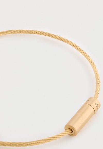 Κολιέ από μέταλλο σε χρυσό τόνο με λεία κυλινδρική κλείσιμο και υφή πλεγμένη, δημιουργώντας έναν κομψό και μινιμαλιστικό σχεδιασμό.