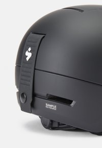 Casco negro con un acabado mate suave. Incluye una correa resistente, aberturas de ventilación y una etiqueta de muestra, enfatizando el diseño de seguridad.
