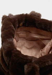 Interiøret i den brune faux fur håndtaske har en glat, lys brun foring med et subtilt log mønster og en lille lommepose til labels.