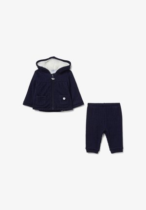Sweat à capuche en maille navy avec doublure en fourrure et poches avant, accompagné d'un pantalon en maille assorti. Fermeture zippée et détail d'accent circulaire.