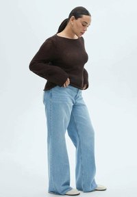 Brun, texturerad stickad tröja med trumpetärmar, kombinerad med ljusblå, vida jeans och vita sneakers. Enkla, avslappnade kläder med kontrasterande texturer.