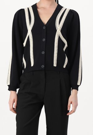 Schwarze Strickjacke mit V-Ausschnitt, verziert mit cremefarbenen Häkelmustern und sechs schwarzen Knöpfen, akzentuiert durch Puffärmel.