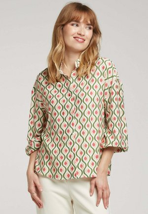 Chemise à motifs avec un devant à boutons, arborant un design ondulé rose et vert sur un fond clair. Manches longues retroussées aux poignets.