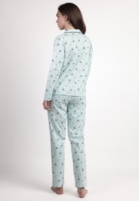 Conjunto de pijama verde menta con mangas largas y pantalones, que presenta un patrón de pequeños pingüinos. Hecho de tela suave, con un corte relajado.