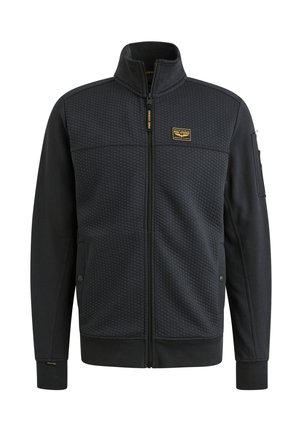 Dark zip-up jacket with a honeycomb textured front, smooth sleeves, zippered pocket on arm, and a logo patch on chest.