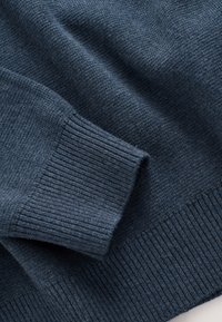 Dunkelblauer gestrickter Pulloverstoff, der Bündchen und Bund mit gerippter Struktur und feinem Strickmuster zeigt.