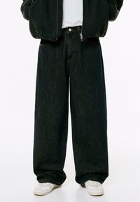 Jeans in denim scuro a gamba larga con finitura testurizzata, dotati di vita alta e tasche frontali, abbinati a sneakers bianche.