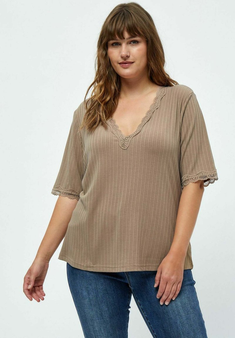Top beige con righe, scollatura a V e ornamento in pizzo sulle maniche. Vestibilità ampia, maniche corte, texture liscia, abbinato a jeans blu.