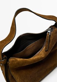Borsa a mano in suède marrone con chiusura a zip, dettagli in pelle liscia e una sola tracolla. L'interno presenta un'etichetta in pelle con il marchio.