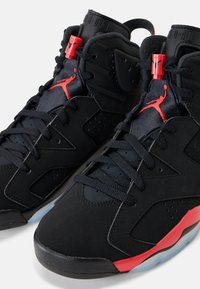 Črni in rdeči visokoplanjski športni copati Air Jordan s črnimi vezalkami, rdečim logotipom Jumpman na jezičku in prozornimi podplati.