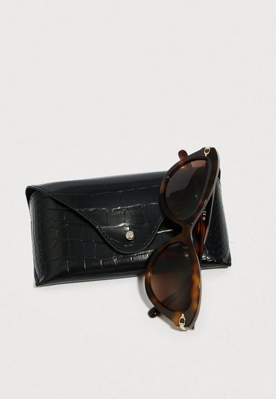 Sončna očala s školjčnim vzorcem in temnimi stekli ob črni škatli s teksturo krokodila in zapiranjem na pritrditev.
