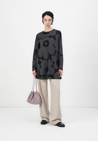 Black tunic with large gray floral patterns, paired with light beige wide-leg trousers. Carrying a small lavender drawstring bag, wearing black shoes.