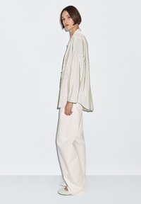 Jasnozielona, w paski, oversize'owa koszula wykonana z gładkiej tkaniny; w zestawieniu z szerokimi, kremowymi spodniami oraz miękkimi, jasnozielonymi kapciami.