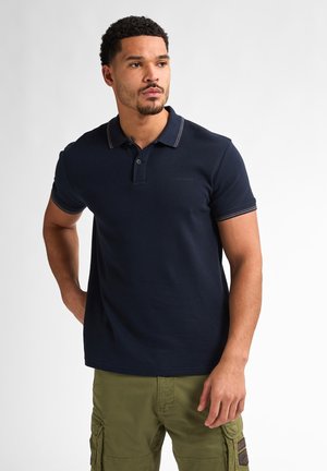 Marineblauwe poloshirt van gestructureerde stof, met een drieknoopsluiting en een contrasterende gestreepte kraag. G gedragen met olijfgroene cargoshorts.