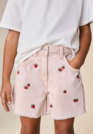 Enfant portant un short en jean rose clair avec de petites fraises rouges brodées et une chemise blanche à manches courtes, mains dans les poches.