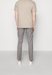 Béžové tričko s kulatým výstřihem a ohrnutými rukávy v kombinaci s kostkovanými kalhotami s červeným a černým vzorem, doplněné bílými teniskami.