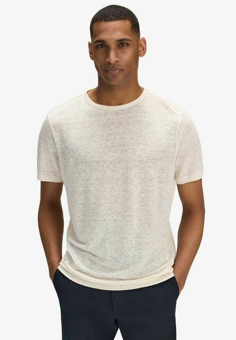 Lys beige kortærmet T-shirt lavet af blødt, struktureret stof. Har en klassisk rund hals og en afslappet pasform. Båret sammen med mørke bukser.