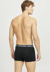 Schwarze Baumwoll-Boxershorts mit einem grauen elastischen Bund, der Logo-Text enthält. Modell von hinten gezeigt, um Passform und Design hervorzuheben.