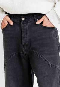 Zwarte denim jeans met een relaxte pasvorm, voorzien van zichtbare stiksels, zijzakken en een knoopsluiting in de taille.