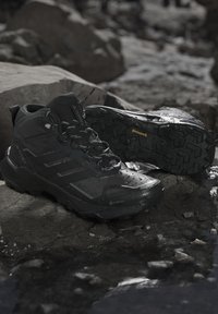 Sorte high-top vandrestøvler med robuste Continental såler på vådt, klippefyldt terræn, med vandtæt Gore-Tex materiale og Terrex branding.