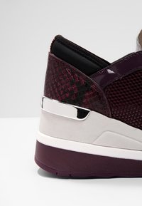 Närbild av lila sneakers klack med strukturerat och nätliknande material, vit mellansula och reflekterande silverdetalj.