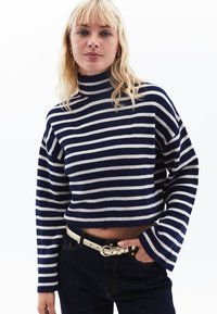 Randig stickad tröja med hög krage, med marinblå och krämfärgade horisontella ränder, kort design och ribbad textur. Kompletterar mörka jeans.