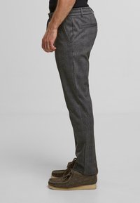 Gray patterned trousers with a tailored fit, featuring side pockets and a smooth texture, paired with brown moccasin-style shoes.