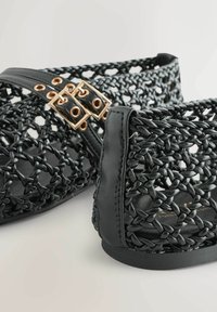 Schwarze geflochtene Sandalen mit einem strukturierten, offenen Design, versehen mit glatten schwarzen Lederakzenten und goldfarbenen Schnallen.