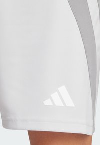 Vita sportshorts med grå sidopanel, slät textur och vit Adidas-logotyp med tre diagonala ränder nära fållen.