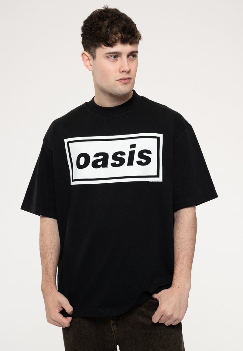 Black oversized t-shirt made of cotton, featuring a bold white rectangular graphic with "oasis" in black lettering. Short sleeves, round neck.