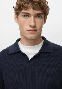 Donkerblauwe ribgebreide polo trui met V-hals en korte kraag, gedragen over een wit T-shirt. Soepele textuur, nauwsluitend ontwerp.