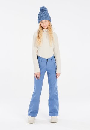 Blauwe sneeuwbroeken van duurzaam materiaal met dubbele zijzakken en een aansluitende tailleband. Gecombineerd met een crèmekleurige zip-up top en een blauwe gebreide muts.