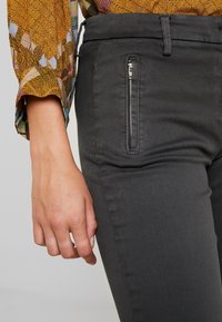 Grå skräddarsydda byxor med en dragkedjeficka på sidan. Tillverkade av mjukt tyg, med en slät struktur och skräddarsydd design.