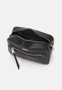 Black leather DKNY bag with gold zippers. Features an external zip pocket and a smooth texture. Rectangular shape with a top handle.