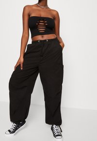 Černý žebrovaný top bez ramínek s vykrojenými detaily, který je kombinován s volnými černými cargo kalhotami s utažením v pase a bočními kapsami.