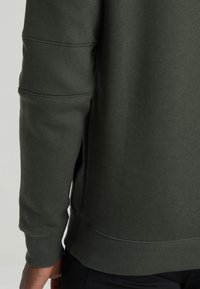 Sudadera verde oscuro con puños y dobladillo acanalados, tejido texturizado con costuras horizontales en la manga y un corte relajado.