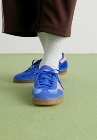 Μπλε και ροζ αθλητικά παπούτσια από σουέτ και μεσέν, με καουτσούκ σόλα και λεπτομερή κορδόνια, σε συνδυασμό με λευκές ριγέ κάλτσες.