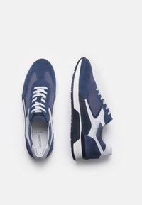 Sneaker blu navy con materiali in suede e mesh, lacci bianchi e suola in gomma texturizzata. Presentano un design elegante e moderno con accenti a contrasto.