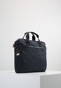 Sort nylon laptop taske med dobbelt topgreb, lynlåslukning, frontlomme og en dekorativ charme. Har en glat, struktureret overflade.