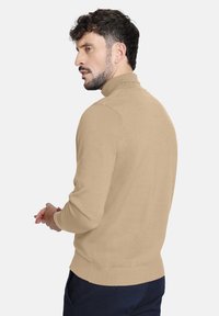 Suéter de punto beige con cuello alto, mangas largas, puños y dobladillo acanalados, textura suave y diseño minimalista, visto desde la parte de atrás.