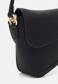 Borsa a tracolla in pelle nera con superficie strutturata, angoli arrotondati e dettagli in metallo dorato. Presenta una chiusura a patta e una tracolla regolabile.