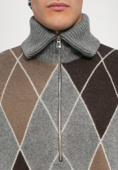 Suéter de punto gris con un alto cuello acanalado, cierre de cremallera y patrón de diamante en tonos de marrón, gris y blanco. Textura suave.