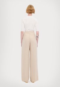 Pantaloni beige a gamba larga realizzati in un materiale morbido, con vita alta e cuciture rifinite. La vista posteriore mostra una silhouette liscia e sartoriale.
