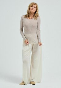 Långärmad, ljusbeige topp med en figurnära kropp och vida vita byxor. Har mjukt tyg, avslappnad passform och platta, vävda slip-on skor.