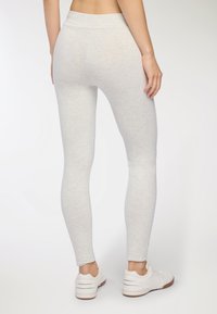 Jasnoszare legginsy wykonane z miękkiego, elastycznego materiału o gładkiej fakturze, z wysokim stanem, w połączeniu z białymi butami sportowymi.