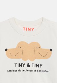 Col blanc de chemise avec deux visages de chiens souriants joints aux oreilles au-dessus du texte "TINY & TINY" et "services de jardinage et d'entretien."