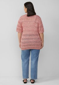 Rood en wit gemêleerd gebreide top met korte mouwen, gecombineerd met losse blauwe jeans en zwarte sandalen, gezien vanaf de achterkant tegen een grijze achtergrond.