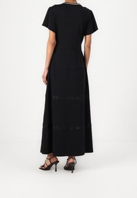 Musta maxi-mekko, jossa on lyhyet lepakkohihat. Mekossa on teksturoituja vaakaraitoja ja istuva vyötärö. Yhdistetty mustiin, naruilla varustettuihin korkokenkiin.