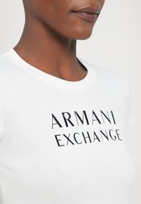 Hvit bomulls T-skjorte med svart trykt logo "ARMANI EXCHANGE." Korte ermer med rund hals og glatt tekstur.