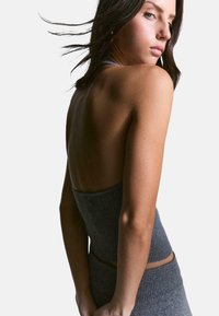 Šedý rebrovaný crop top s nízkym dizajnom na chrbte, priliehavým strihom a jemnými priehľadnými detailmi. Hladká textúra a aerodynamický strih.